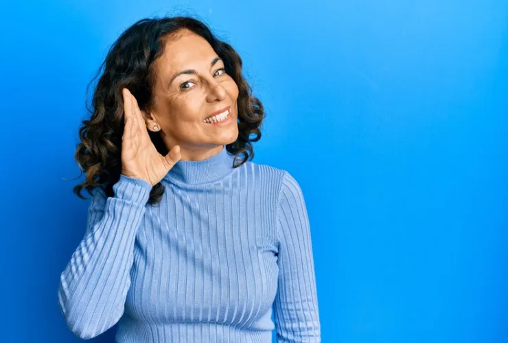 Idosa sorrindo enquanto ajusta um aparelho auditivo no ouvido