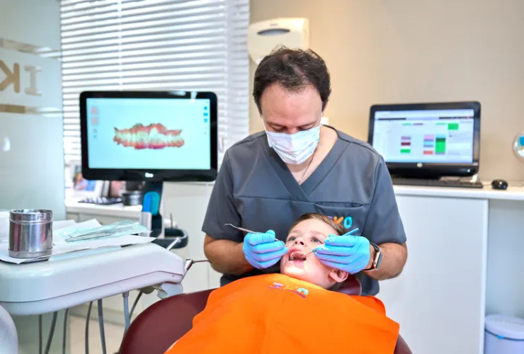 Criança sorrindo durante consulta odontológica, com aparelho dentário infantil, representando o tratamento ortodôntico precoce.