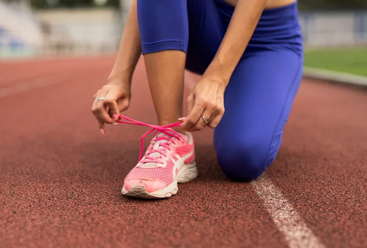 Corredor amarrando o tênis antes do treino, representando os cuidados essenciais com os pés para prevenir lesões.