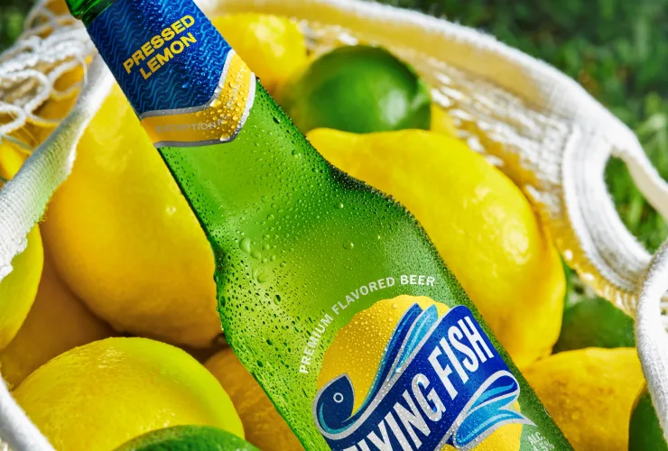 Garrafas e latas da cerveja Flying Fish mostrando embalagem com rótulo azul-claro e destaque para “limão” e “baixo amargor”.