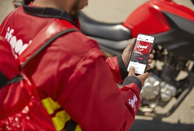 Entregador usando aplicativo do iFood no celular escolhendo rota de entrega