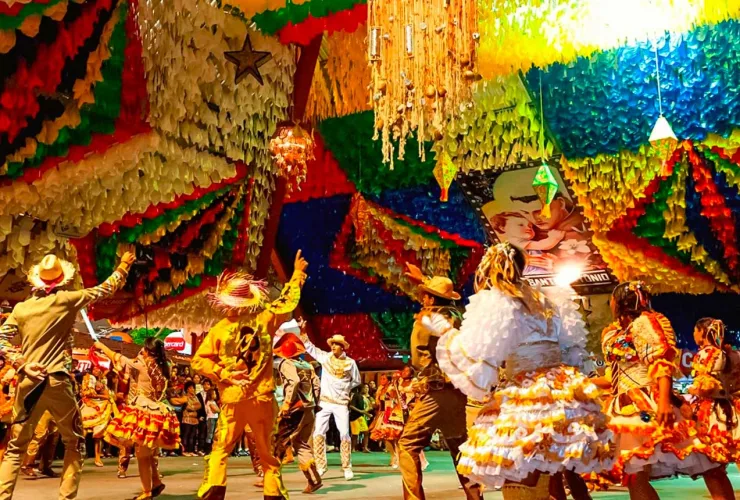Imagem representando festas juninas no Brasil com bandeirinhas, fogueira e público em celebração típica do São João