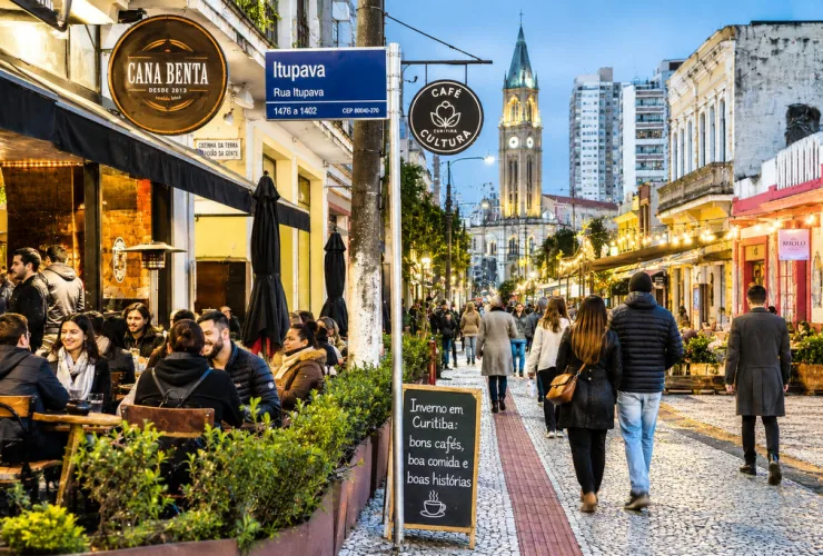 Pessoas circulando entre restaurantes, cafés e eventos culturais durante uma noite de inverno em Curitiba.