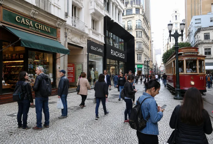 Fachada de uma antiga loja familiar no centro de Curitiba ao lado de uma grande rede varejista moderna, com consumidores utilizando smartphones para compras online.