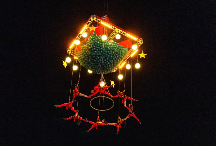 Artistas de balé aéreo em figurinos vermelhos se apresentam sob estrutura natalina iluminada