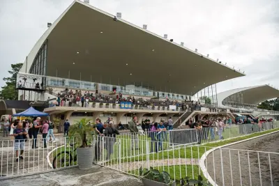 Pessoas assistindo corridas no Jockey Club do Paraná com arquibancada e área ao ar livre.