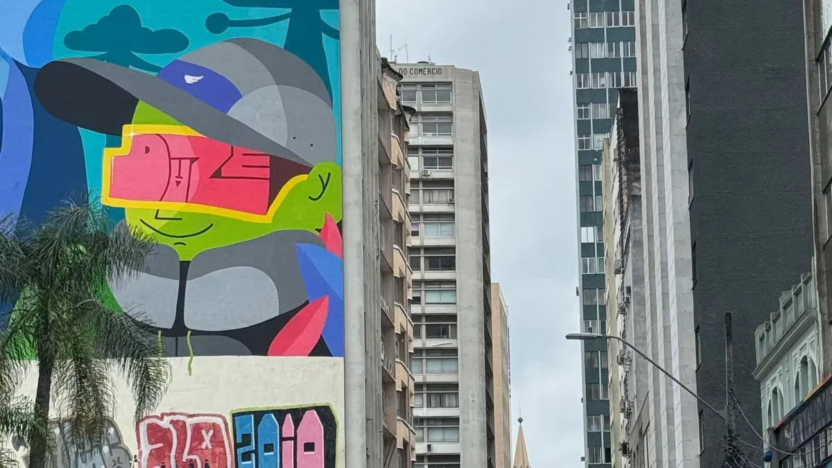 Mural colorido com figura estilizada de gralha-azul usando boné e óculos, em parede lateral no Centro de Curitiba.