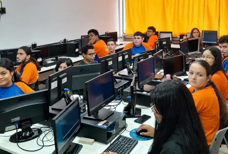 Sala de informática com jovens sentados em frente a computadores participando de aula no Instituto Forja