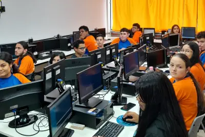 Sala de informática com jovens sentados em frente a computadores participando de aula no Instituto Forja