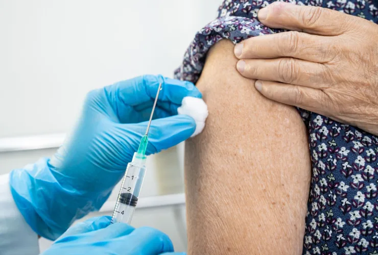 Profissional de saúde com luvas azuis aplica vacina no braço de uma pessoa idosa