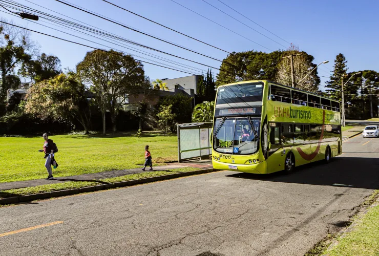 Ônibus de dois andares da Linha Turismo de Curitiba em rua arborizada.