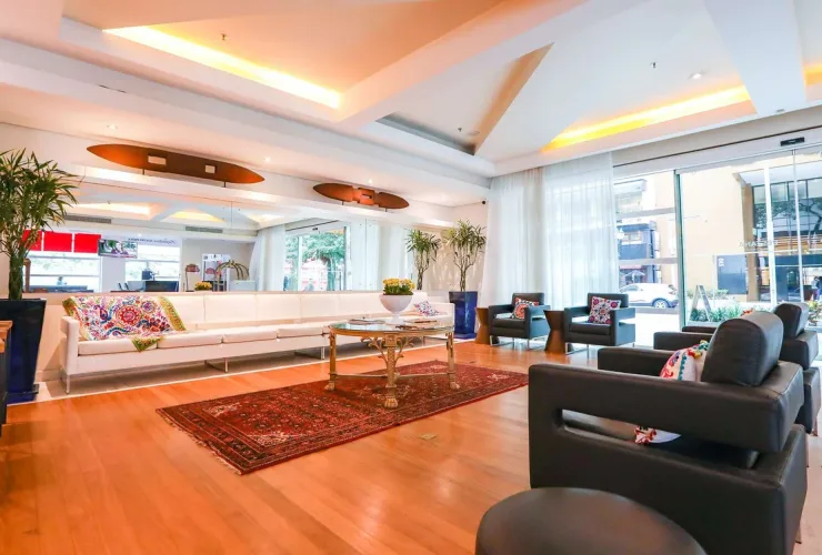 Lobby de entrada do Pestana Curitiba, no Batel, com poltronas, sofá branco e mesa de centro