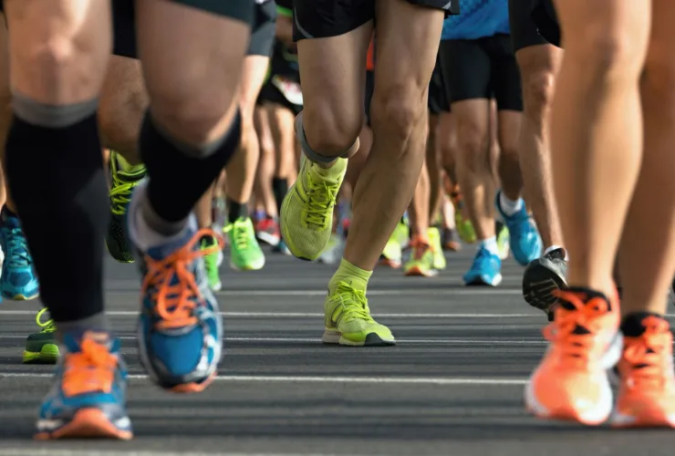 Pernas de corredores com tênis coloridos durante uma prova de corrida de rua no asfalto