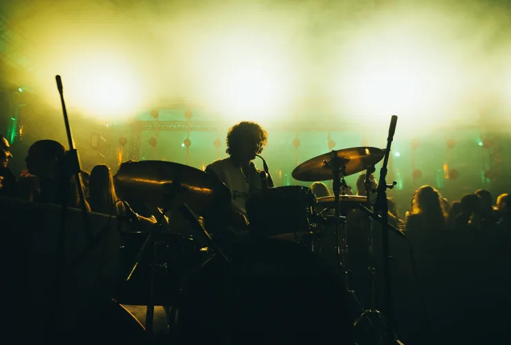 Baterista durante apresentação do Syon Trio, sob iluminação amarela e verde.