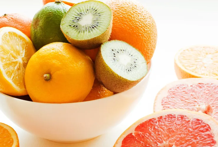 Tigela com laranjas, limão e kiwis cortados, ao lado de fatias de toranja