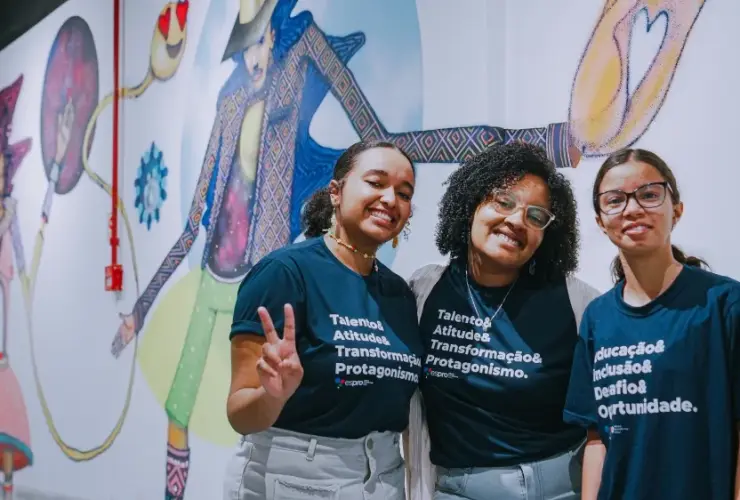Três jovens sorrindo vestindo camisetas do Espro em frente a mural colorido.