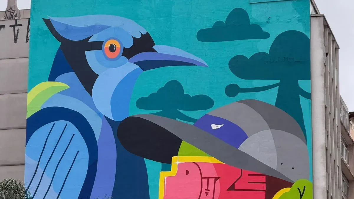 Mural colorido no Centro de Curitiba com uma gralha-azul estilizada e elementos gráficos abstratos em tons de azul, cinza e rosa.