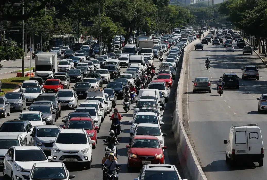 Rodovia com trânsito intenso de carros e motos em um dos sentidos e fluxo livre no sentido oposto.