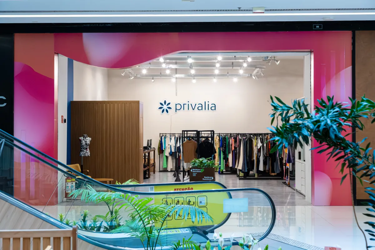 Loja temporária da Privalia em shopping de Curitiba com roupas expostas e escada rolante à frente